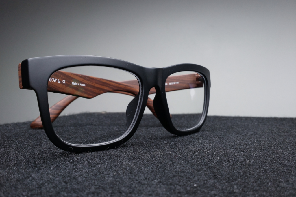 Close-up of black-rimmed eyeglasses with wooden temples placed on a dark surface.