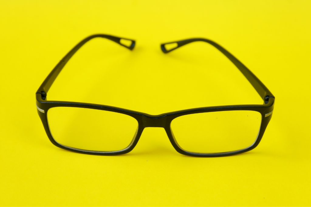 Front view of black eyeglasses with rectangular frames placed on a yellow background.