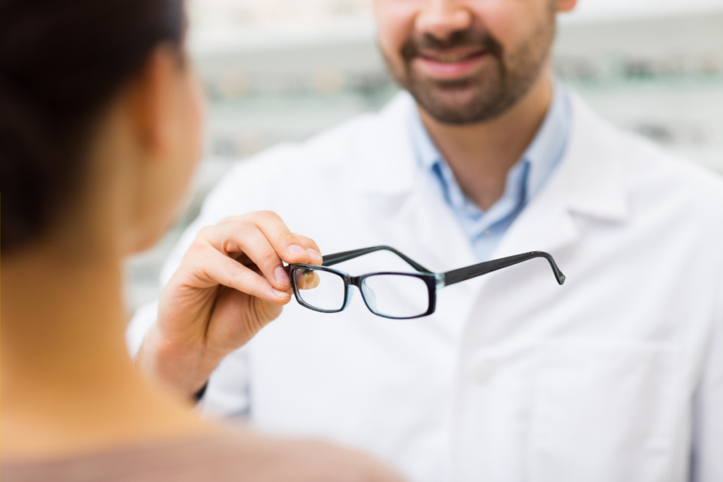 An optician holding a pair of eyeglasses and presenting them to a customer.