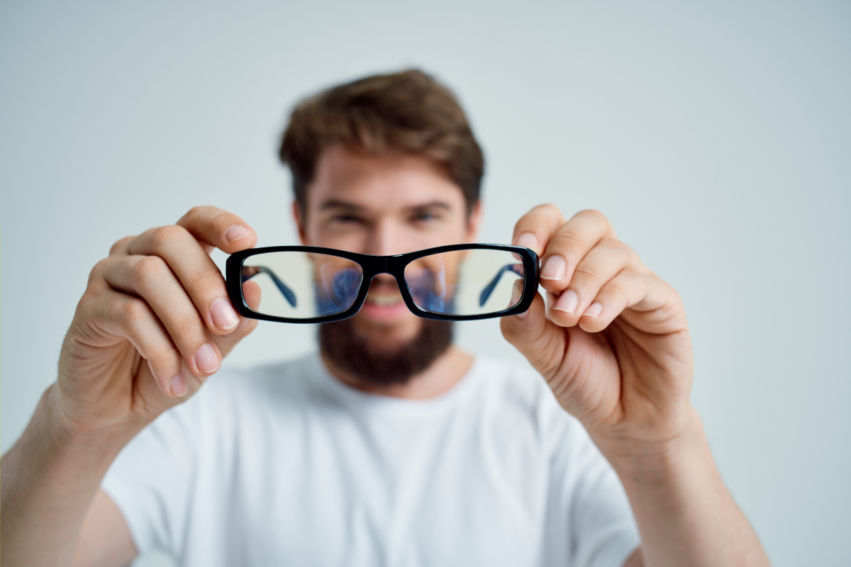 A man holding black-rimmed glasses in front of the camera, smiling in the background.