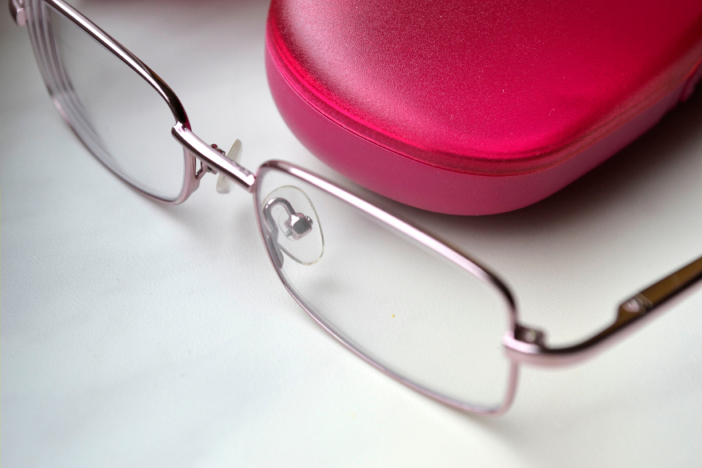 Close-up of rectangular eyeglasses with a pink frame placed next to a red eyeglasses case.