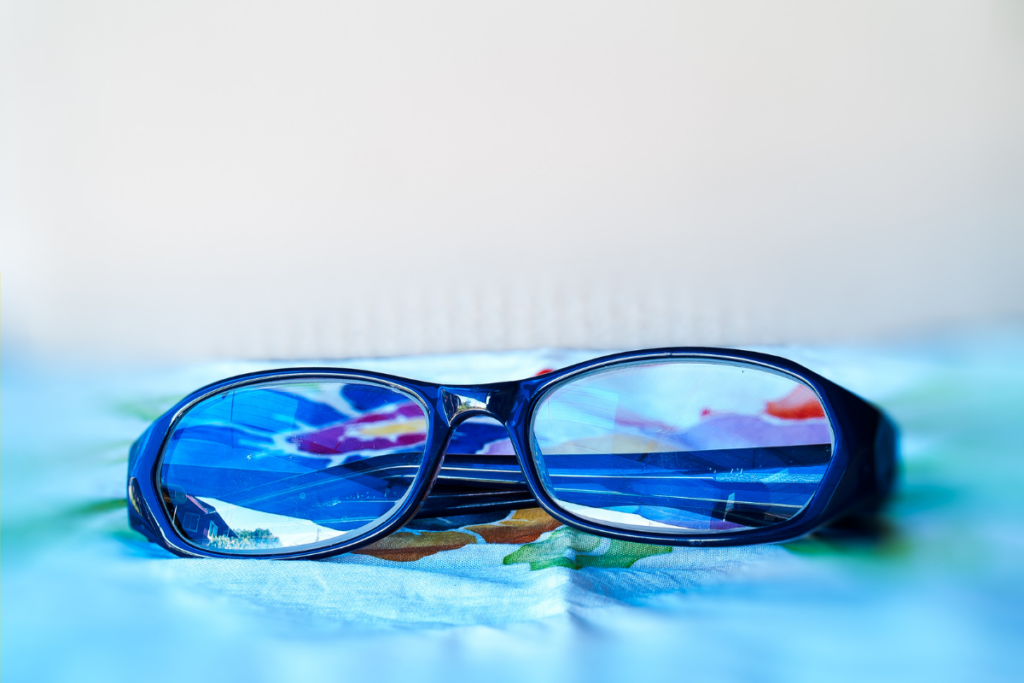 Blue rectangular eyeglasses with reflective lenses placed on a colorful surface.