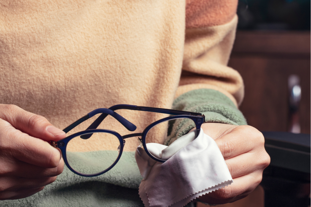 A person cleaning a pair of blue eyeglasses with a white microfiber cloth.