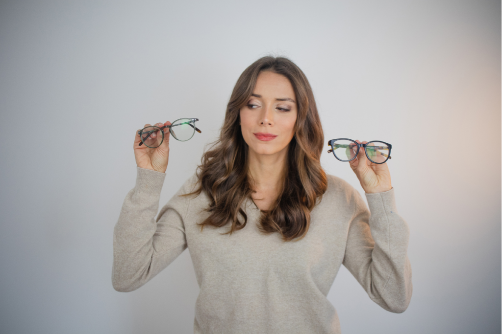 A person’s hand reaching for a pair of eyeglasses on a display rack in an optical store.