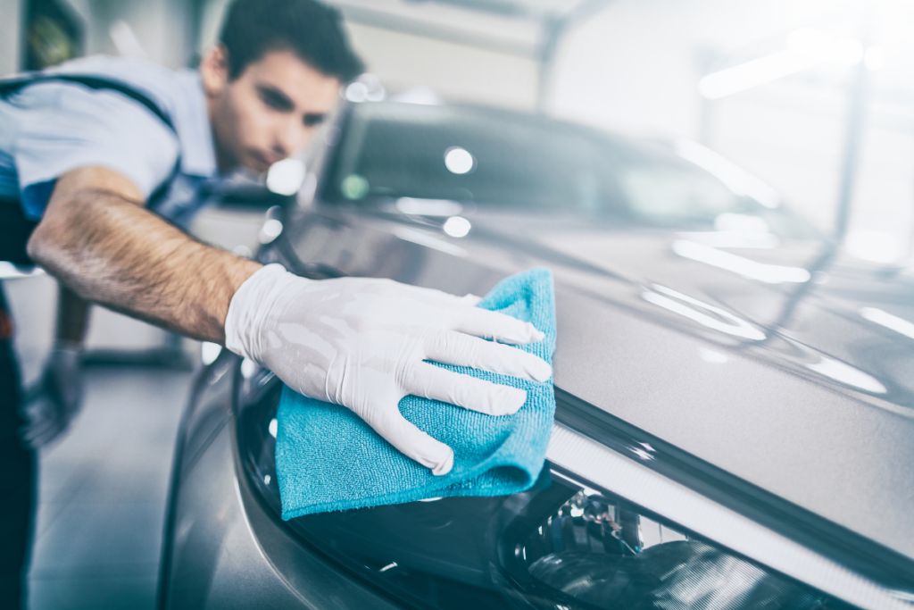 Man wearing gloves polishing the exterior of a car with a blue microfiber cloth.
