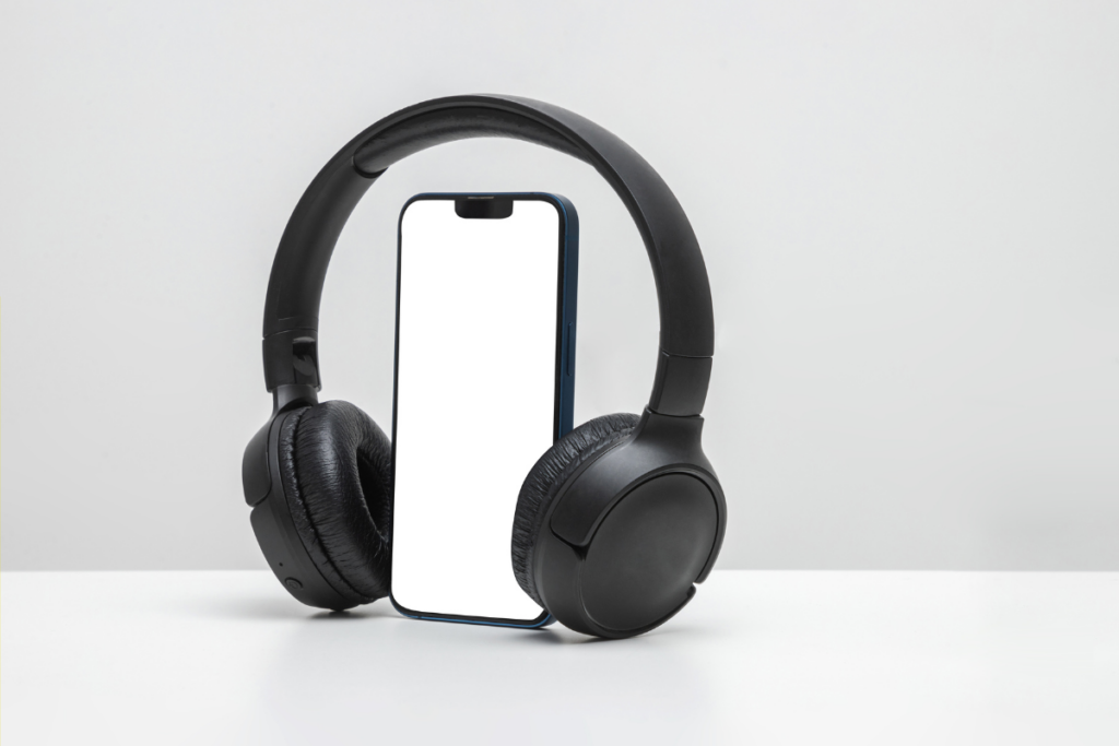 Smartphone placed inside a pair of black over-ear headphones, creating a minimalist composition on a white surface.