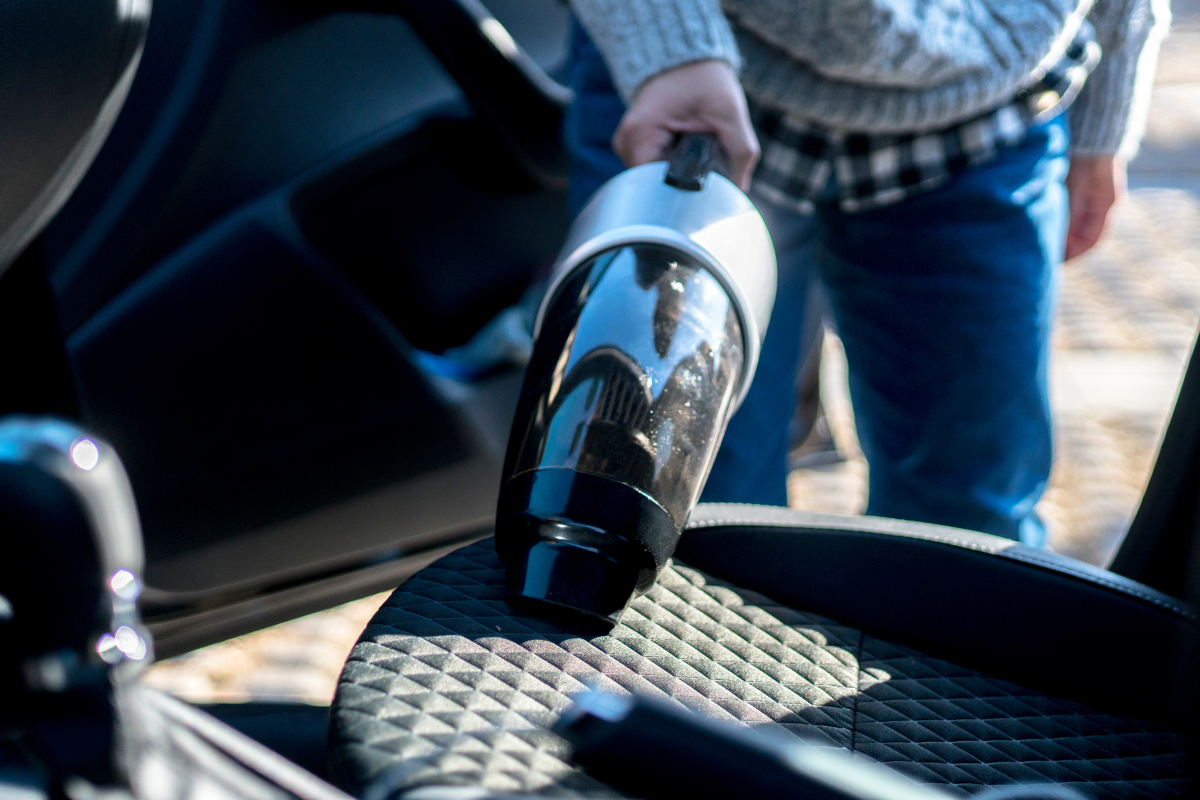 A person using a portable handheld vacuum cleaner to clean the fabric seat of a car.