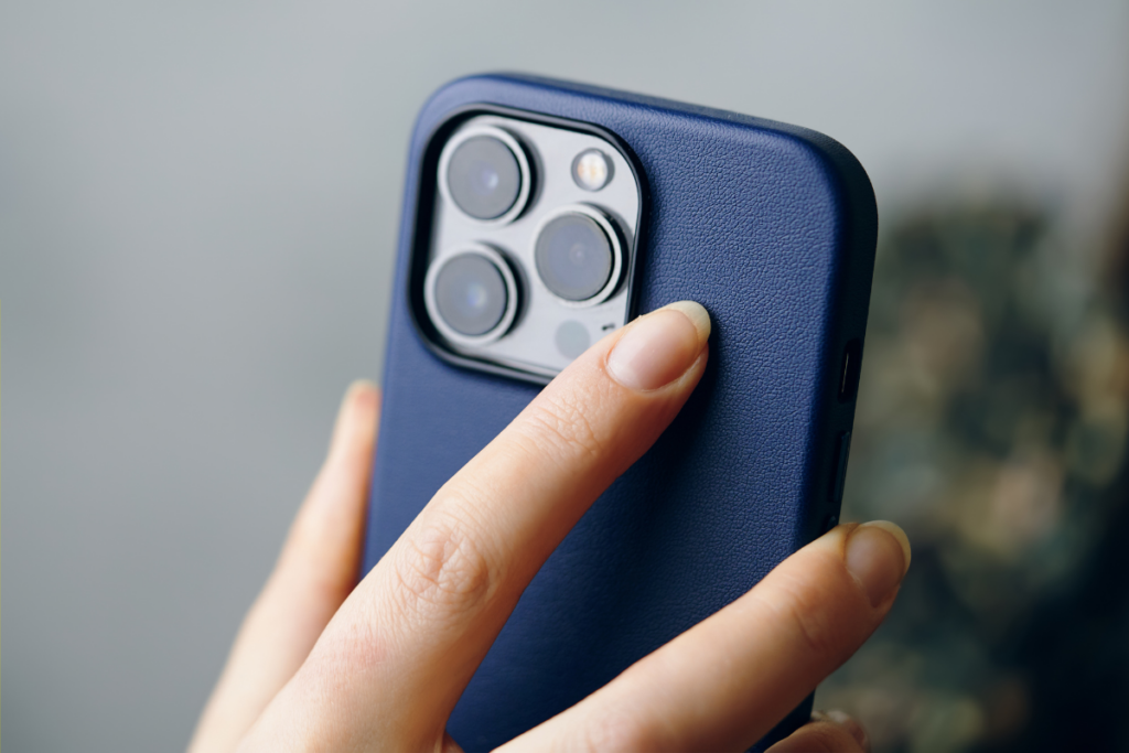 Close-up of a person holding a smartphone with a dark blue case, focusing on the triple camera lenses at the back.