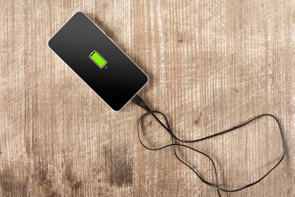 Smartphone connected to a charging cable on a wooden surface, displaying a battery charging icon at 50%.