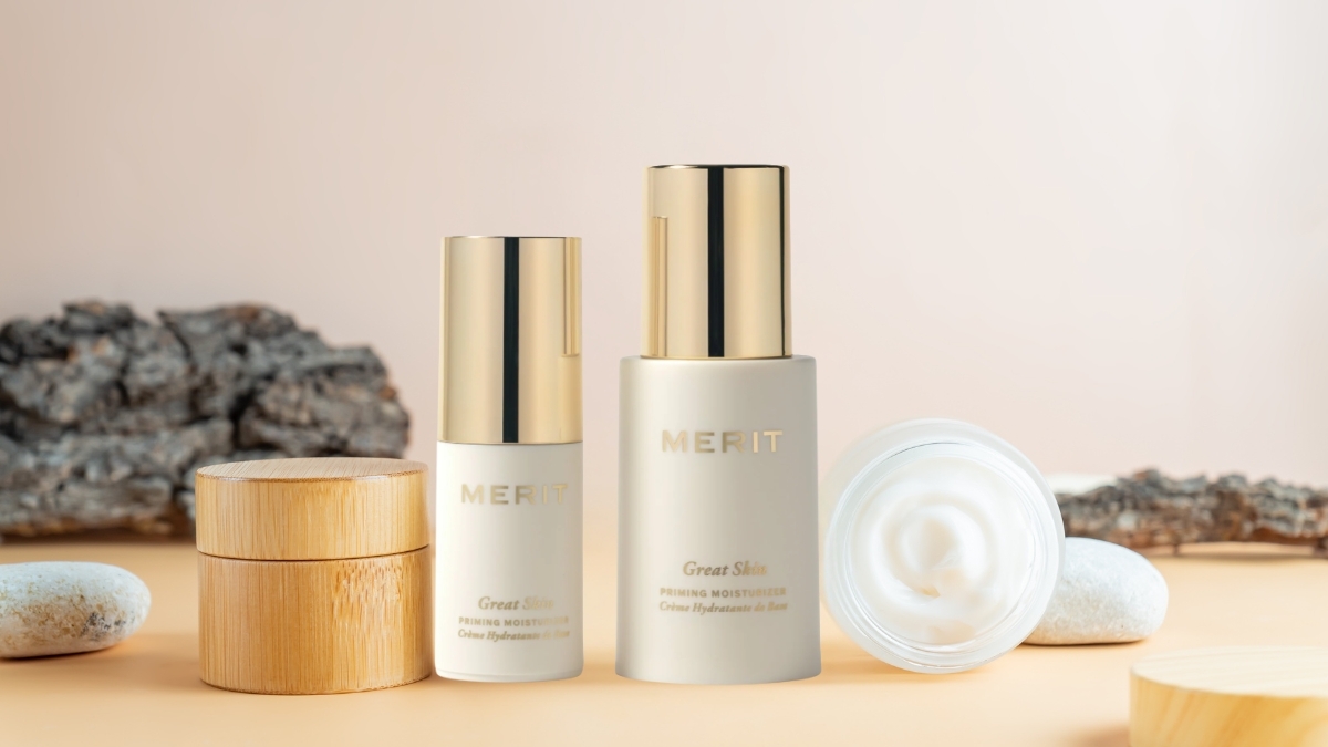 MERIT Great Skin Priming Moisturizer bottles and open cream jar displayed with natural wood and stone accents on a soft beige background.