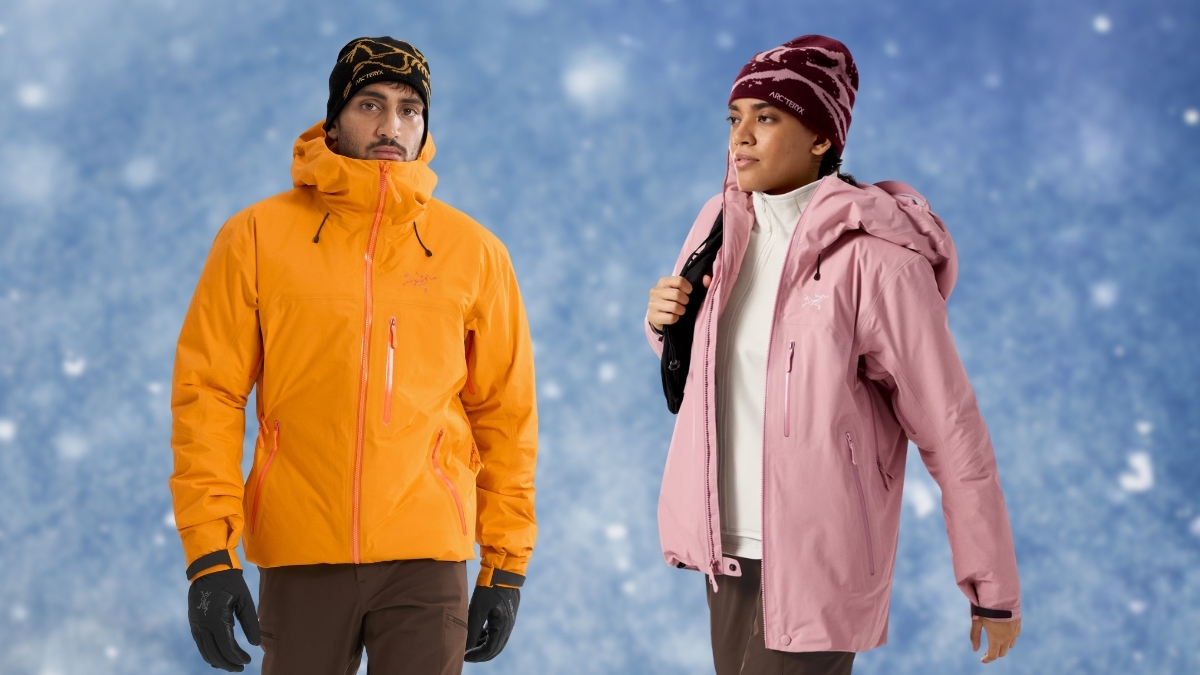 Two people wearing Arc'teryx winter jackets—one in bright orange and one in light pink—standing against a snowy blue background, showcasing premium outdoor gear featured in The Ultimate Arc'teryx Gift Guide.