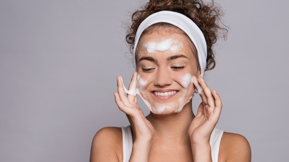 Woman cleansing her face with a foaming facial cleanser while smiling during her skincare routine