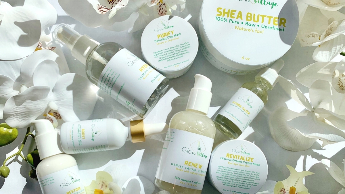 Glow Village skincare products flat lay featuring shea butter, facial cleansers, hydrating serums, clay masks, and moisturizers surrounded by white orchids.