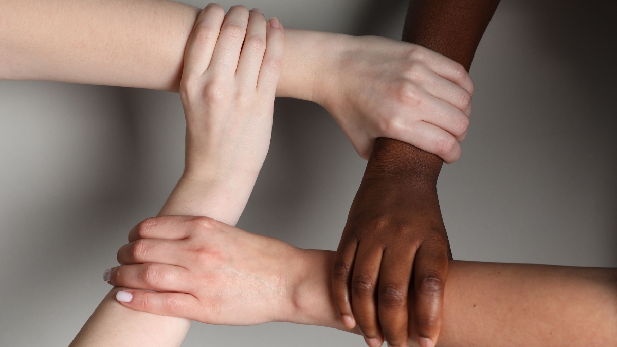 Hands of people with different skin tones linked together in a circle, symbolizing unity, diversity, and racial equity.