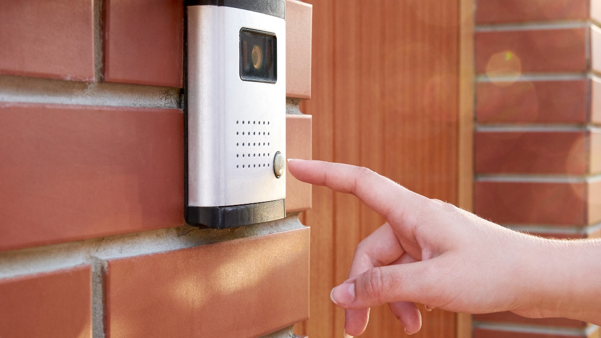 Person pressing the button on a video doorbell installed on a brick wall, representing home security and smart entry systems.