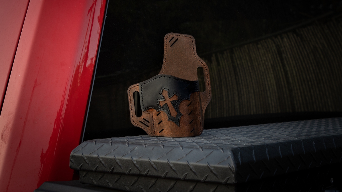 Brown and black leather 1911 holster with cross design resting on a truck toolbox, showcasing handcrafted firearm holster detail.