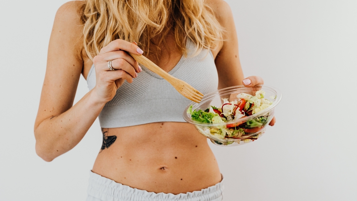 Woman holding a fresh vegan salad bowl and eating with a wooden fork, promoting healthy plant-based eating and lifestyle.