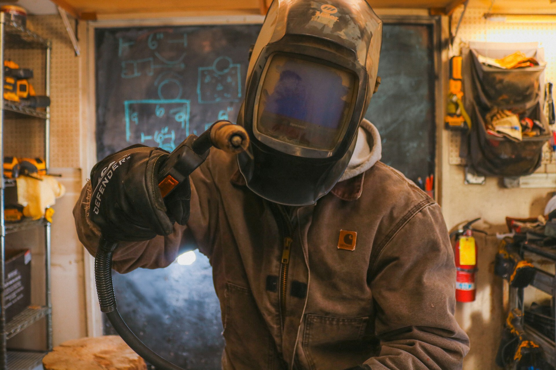Welder wearing a Carhartt work jacket and protective gear while working in a workshop.